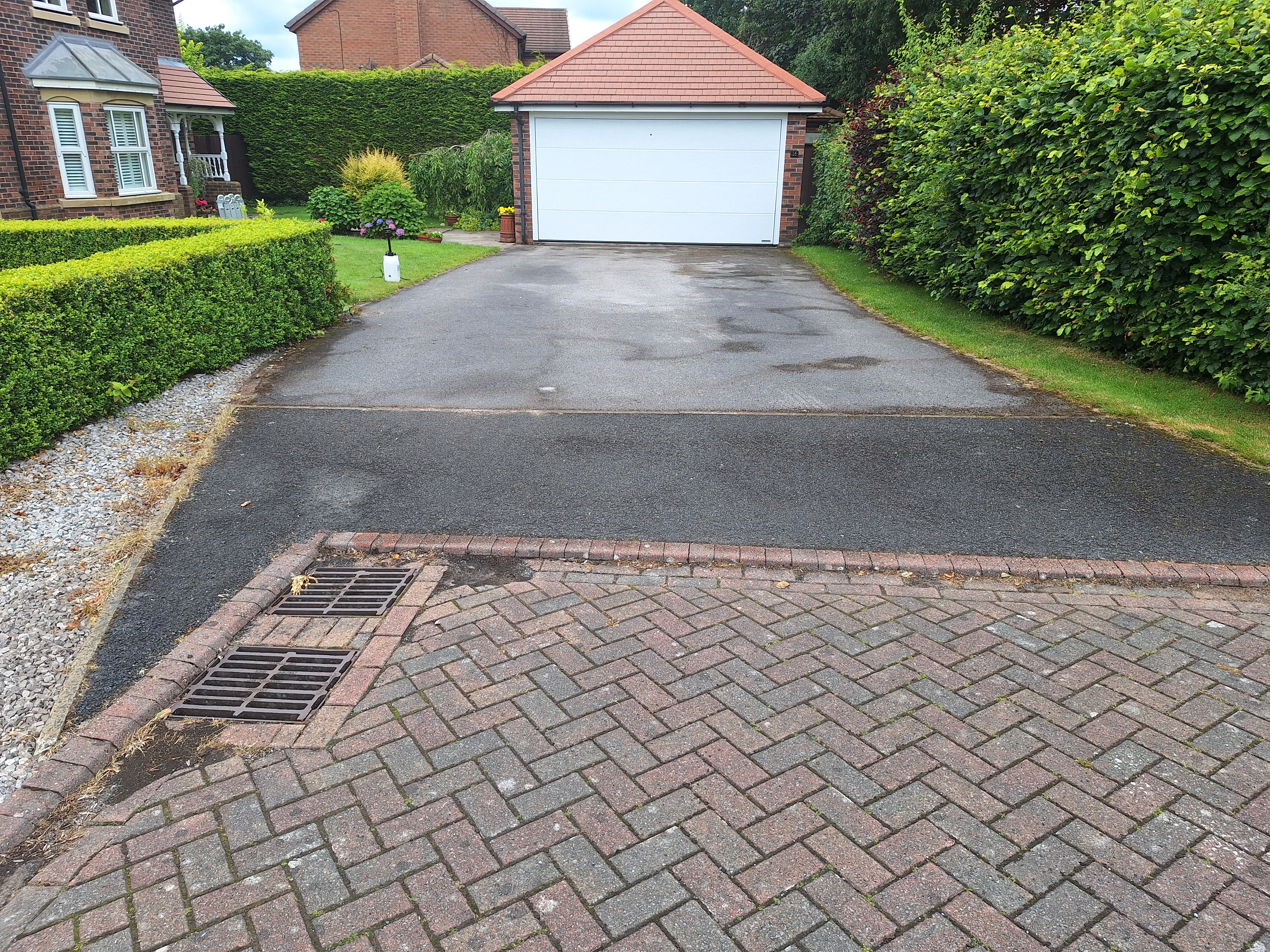 Tarmac driveway before restoration, with a faded and uneven surface leading to a white garage door.